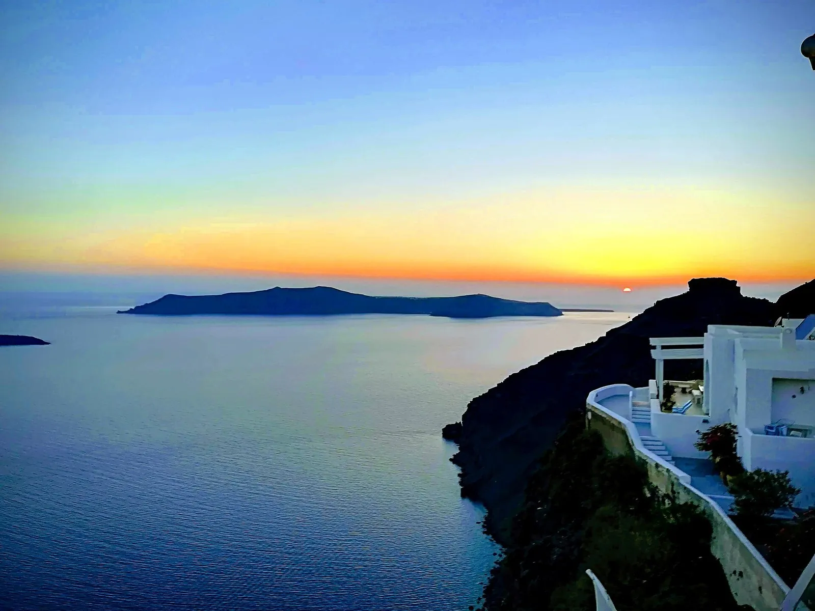 Golden sunset over the caldera seen from a cliff-top terrace, the evening a Santorini honeymoon is planned around