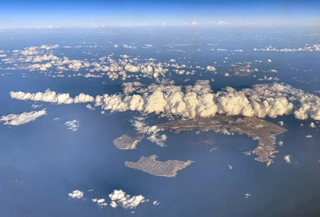 Aerial view of the Santorini island group under scattered clouds, with Thirasia and Aspronisi in the foreground