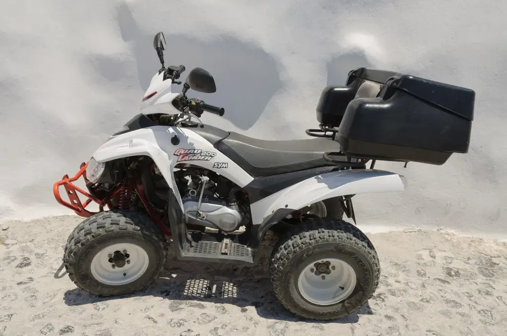 A white and black quad bike with a rear storage box parked against a whitewashed wall