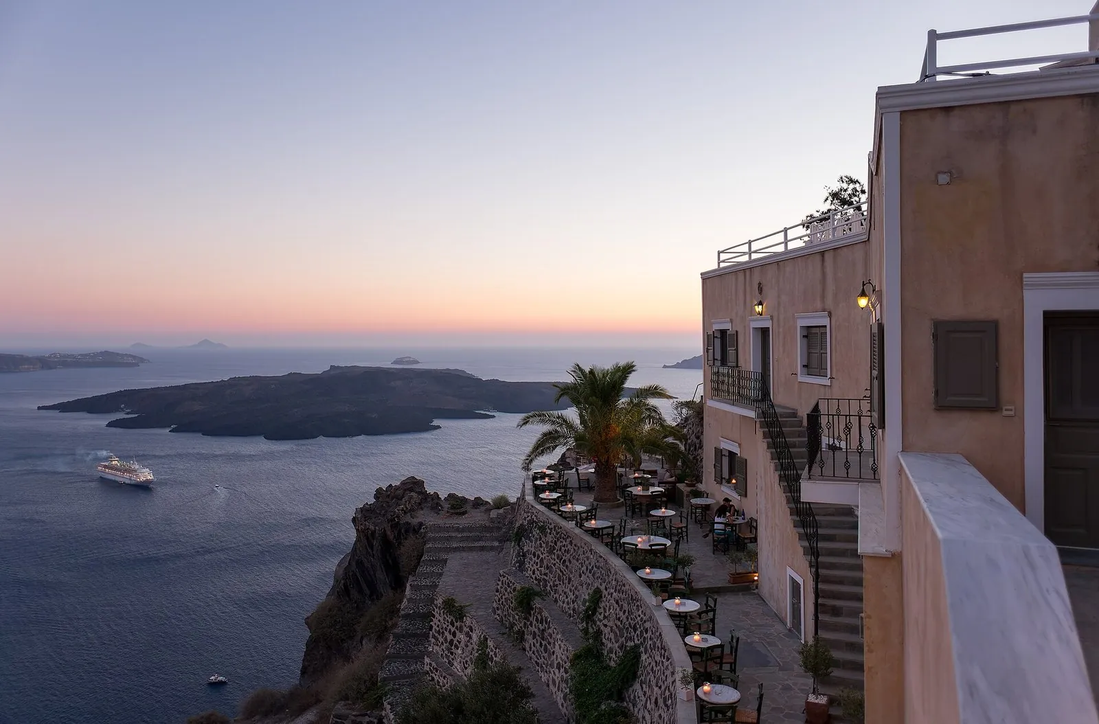 Santorini restaurants on terraces down the Fira cliff at dusk, looking over the caldera to Nea Kameni