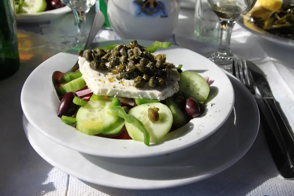 Greek salad with cucumber, peppers, olives, a slab of white goat cheese and capers on top