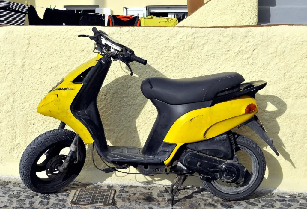 A yellow and black scooter parked on a cobbled lane against a cream wall