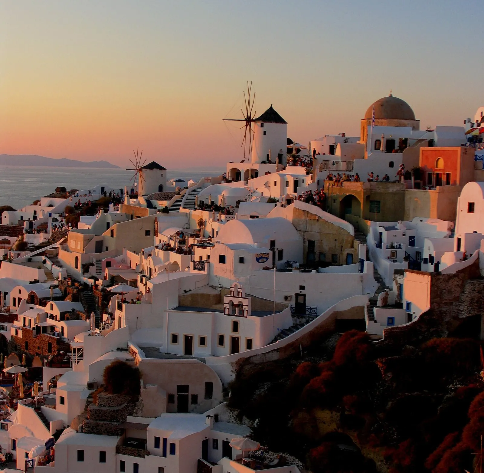 Oia's white houses and windmills glowing in the last light of a Santorini sunset above the caldera