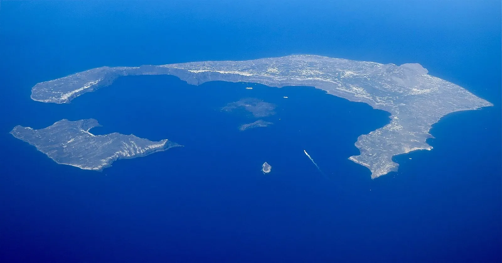 Aerial view of the Santorini volcano: a broken ring of islands around a flooded caldera with two dark volcanic islets in the middle