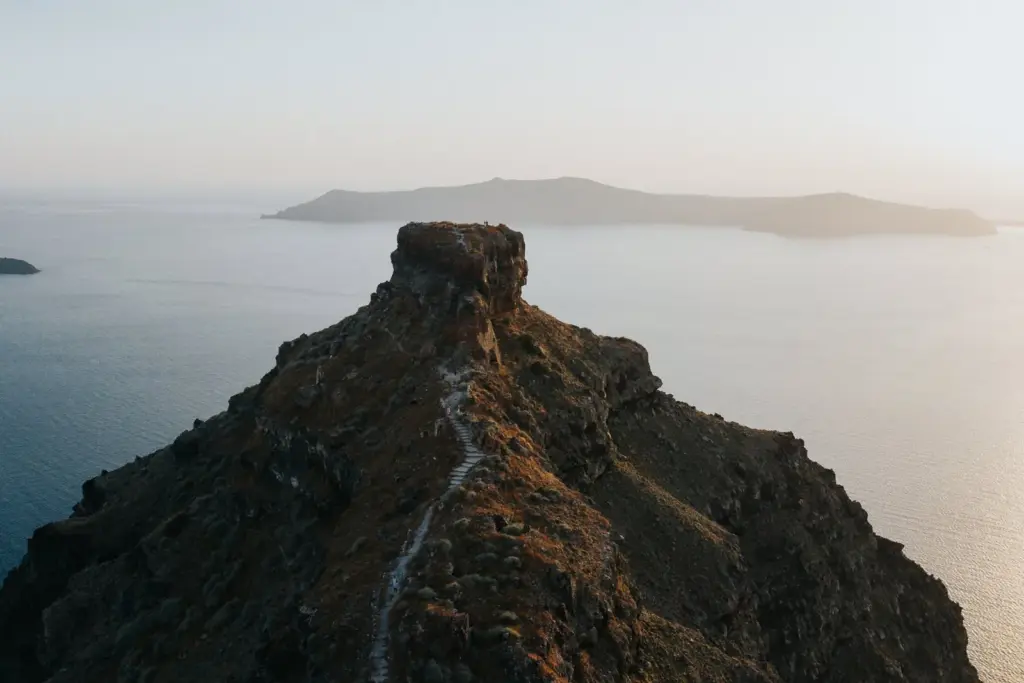 Skaros rock jutting into the calm caldera at sunset, with a footpath along its ridge and Thirasia beyond