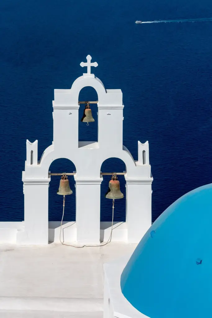A white triple bell gable with three bronze bells above a blue dome, against the deep blue sea