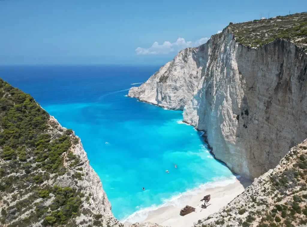 A white-sand cove with a rusting shipwreck below sheer limestone cliffs and turquoise water at Navagio